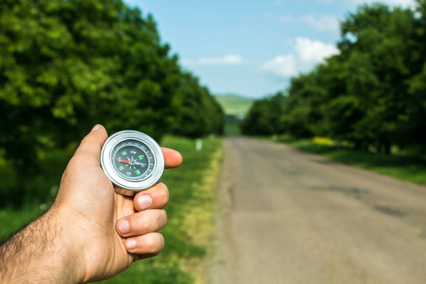 holds a compass on the background of the road and trees - 写真・画像