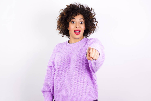 Excited positive   young beautiful hispanic  woman wearing sweater    points index finger directly at you, sees something very funny. Wow, amazing - 写真・画像