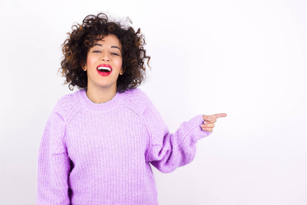 молода красива латинка в светрі сміється щасливо вказує на порожній простір демонструє пропозицію про купівлю зі знижкою, схвильовану хорошими новинами або несподіваними продажами. - Фото, зображення