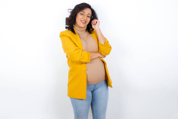 Cheerful  pregnant businesswoman wearing yellow blazer with hand near face. Looking with glad expression at the camera after listening to good news. Confidence. - Valokuva, kuva