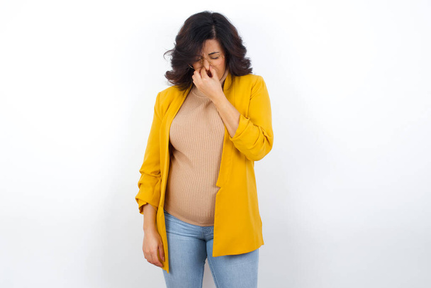 femme d'affaires enceinte portant un blazer jaune tenant son nez à cause d'une mauvaise odeur. - Photo, image