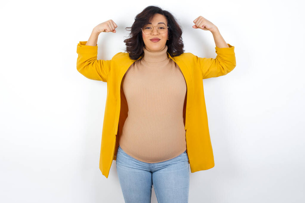 Waist up shot of pregnant  woman raises arms to show muscles feels confident in victory, looks strong and independent, smiles positively at camera. Sport concept. - Photo, Image