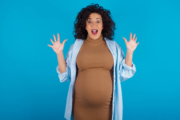 Optimistic pregnant arab woman raises palms from joy, happy to receive awesome present from someone, shouts loudly, Excited model screaming. - Photo, Image