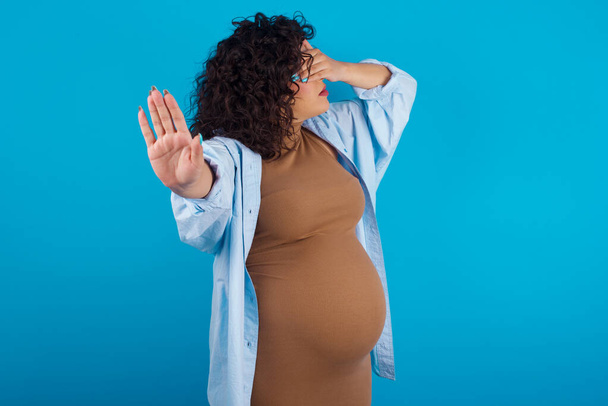 femme enceinte couvre les yeux avec la paume et faire un geste d'arrêt, essaie de se cacher de tout le monde. - Photo, image