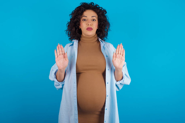 Serious pregnant woman pulls palms towards camera, makes stop gesture, asks to control your emotions and not be nervous - Foto, imagen