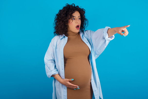  вагітна арабська жінка, вказуючи пальцем здивований попереду, відкритий рот здивований вираз, щось на фронті. - Фото, зображення