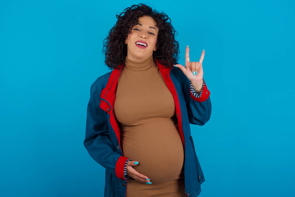 pregnant woman doing a rock gesture and smiling to the camera. Ready to go to her favorite band concert. - Photo, Image