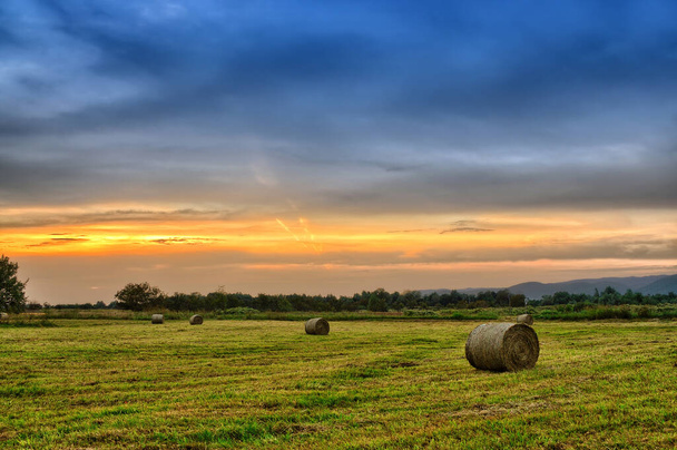 Zlatý západ slunce nad farmářským polem s balíky sena - Fotografie, Obrázek