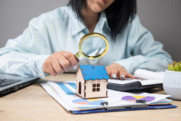 uma mulher olha para a casa com uma lupa e sobre o papel de mesa e dados - Foto, Imagem