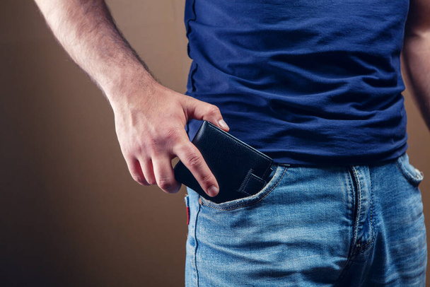 man puts wallet in front pocket on brown background - Photo, Image