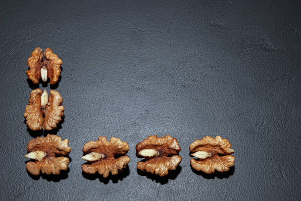geschilde helften van walnoten zonder schil op een grijze achtergrond in de vorm van een frame links en onderaan, gefotografeerd door macrofotografie - Foto, afbeelding