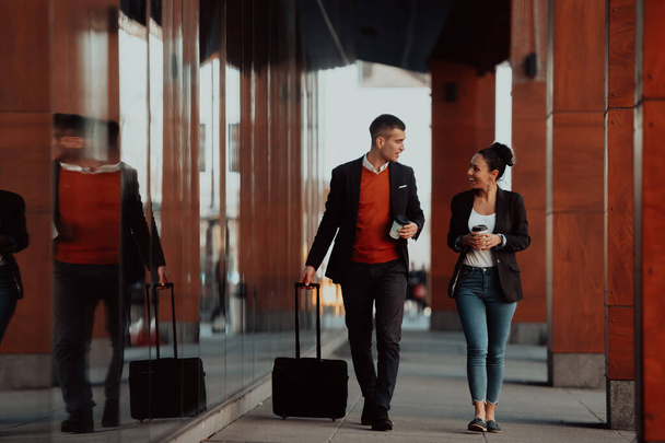 Businessman and businesswoman talking and holding luggage traveling on a business trip, carrying fresh coffee in their hands. Business concept. High-quality photo - Foto, Bild