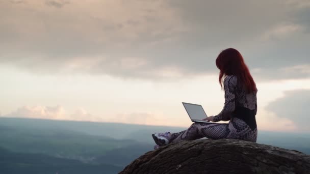 Девушка блоггер Путешественник печатает текст на ноутбуке, сидя на вершине горы - Кадры, видео