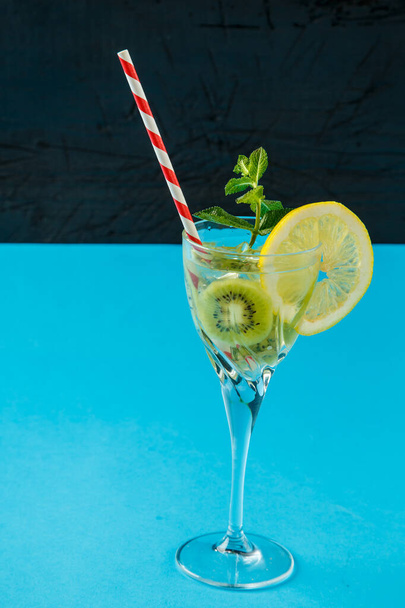 Kiwi cocktail garnished with lemon and mint in a glass on a napkin against a blue background. - Фото, зображення
