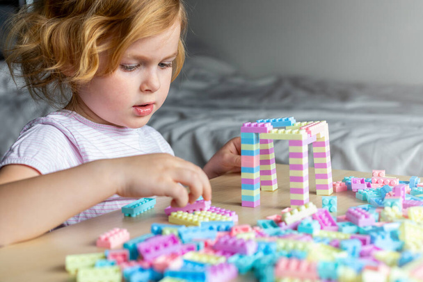 Маленька красива дитина грає з іграшковими пластиковими будівельними блоками, сидячи за столом. Маленька дівчинка зайнята веселою творчою дозвіллям. Розвиток образотворчих рухових навичок для дітей
. - Фото, зображення