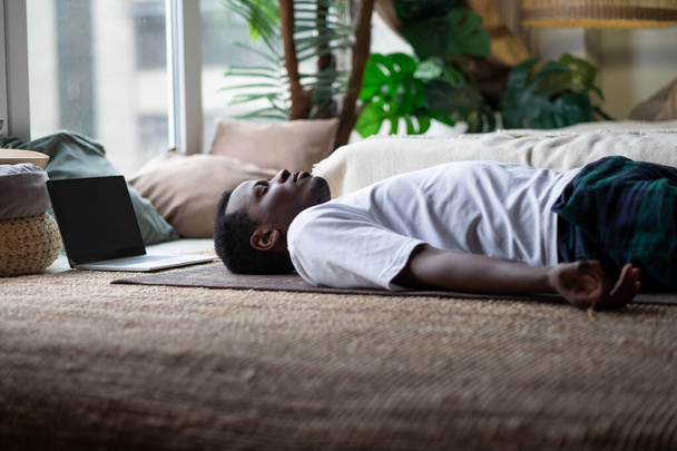 Йога. Африканський молодий чоловік медитує на підлозі і лежить у позі Шавасани.. - Фото, зображення