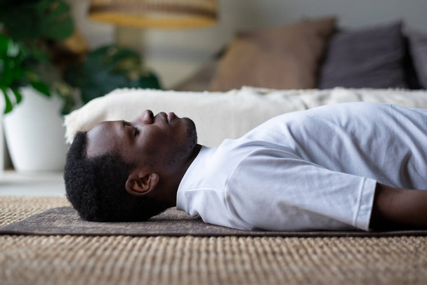 Du yoga. Jeune homme africain méditant sur le sol et couché dans la pose de Shavasana. - Photo, image