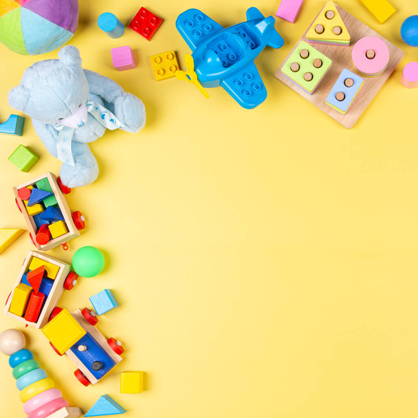 Colorati giocattoli educativi in plastica di legno e soffici per bambini su sfondo giallo pastello. Vista dall'alto, piatta - Foto, immagini