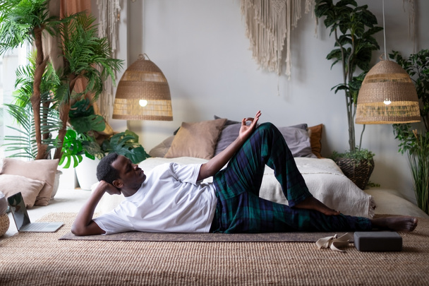 African yoga man doing anantasana pose working out at home - 写真・画像
