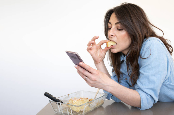Nuori tyttö syö pala kakkua, kun käytät älypuhelinta - Valokuva, kuva