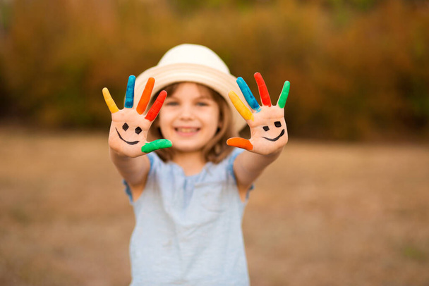 Feliz niña sonriente con las manos pintadas en la cara divertida jugar al aire libre en el parque. Concéntrate en las manos - Foto, Imagen