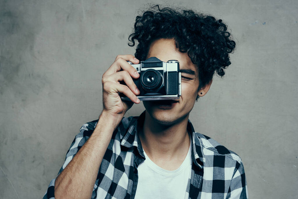 man met een camera in zijn handen op een grijze achtergrond binnen hobby geruite shirt model - Foto, afbeelding