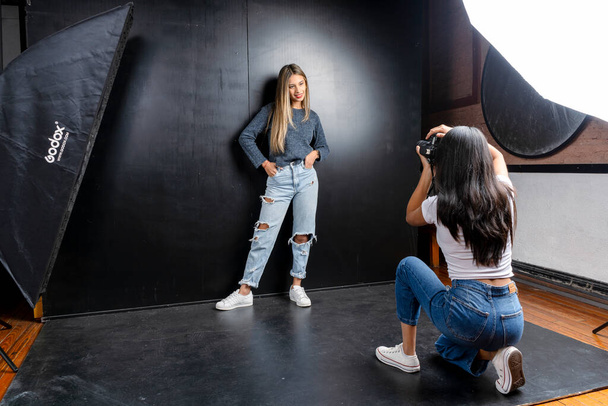 Horizontal portrait of a photo session of a model and a woman photographer in a photography studio, black background. - 写真・画像