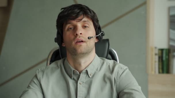 Man in a shirt is using a headset in the office, a man is looking and talking into the camera while sitting at a desk. - Záběry, video