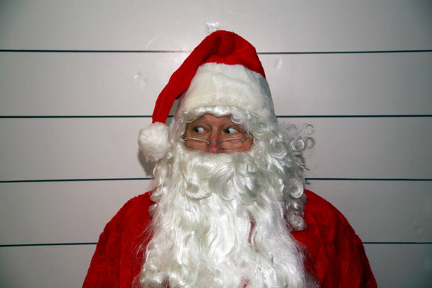 Kerstman Mugshot. De Kerstman heeft een blanco wit boekingsbord terwijl zijn politiefoto wordt gemaakt. Reserveringsbord is leeg voor uw tekst. - Foto, afbeelding