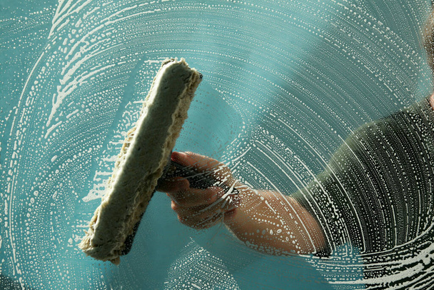  Een man wast ramen met een Squeegee en zeepwater. Een glazenwasser wast en reinigt vieze ramen om ze Squeekie Clean te maken. Raamreiniging.   - Foto, afbeelding