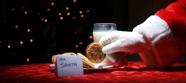 サンタクロースはクリスマスのイブに彼のために残されたミルクとクッキーを楽しんでいます。 - 写真・画像