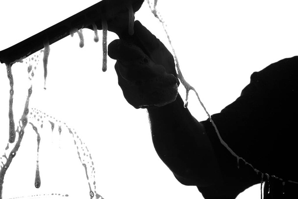 Raam wassen. Een zwart-wit beeld van een Raamreiniger Hand terwijl hij een raam vuil reinigt met zeepwater en een Squeegee. Squeekie Clean Windows terwijl u wacht met een professionele raamreiniging. - Foto, afbeelding