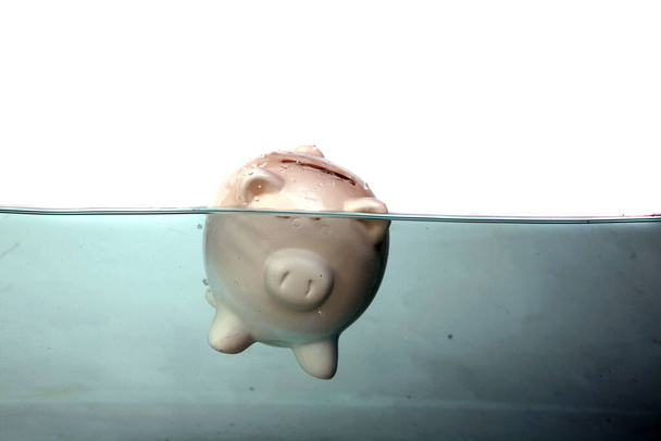 Een Piggy Bank drijft in vuil water. De economie heeft veel mensen het gevoel dat hun financiën hen nauwelijks overeind houden. Geld is krap door een slechte economie. De inflatie neemt toe.  - Foto, afbeelding