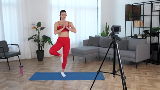 Fit žena fitness trenér blogger medituje, zatímco stojí na podložce jógy doma - Záběry, video