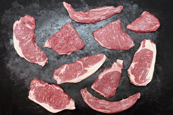 Various Raw Steaks. Sirloin Beef Steaks, Overhead View. Many Raw Striploin Steaks from Marbled Beef on Black Background. Group of Black Angus Beefsteaks. Raw Sirloin Cuts. Uncooked Prime Beef Steaks. - Photo, Image