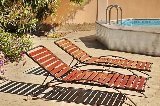 Drewniane fotele lub leżaki w ogrodzie patio przy basenie. Drewniane leżaki lub łóżka deskowe na betonie. Leżaki na podwórku. - Zdjęcie, obraz