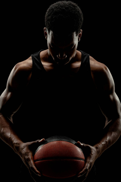 Basketball player holding a ball against black background. Serious concentrated african american man. - Fotografie, Obrázek