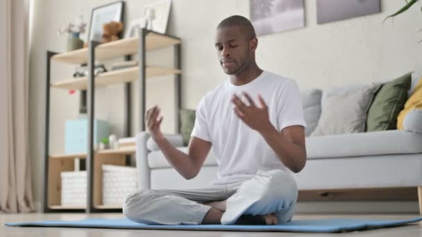 Молодой африканский человек медитирует на коврике для йоги дома - Кадры, видео