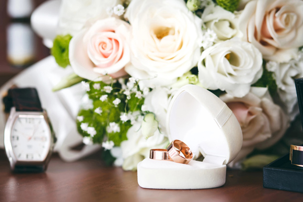 Anillos de boda de oro en caja de regalo blanca en forma de corazón y ramo de boda
. - Foto, Imagen