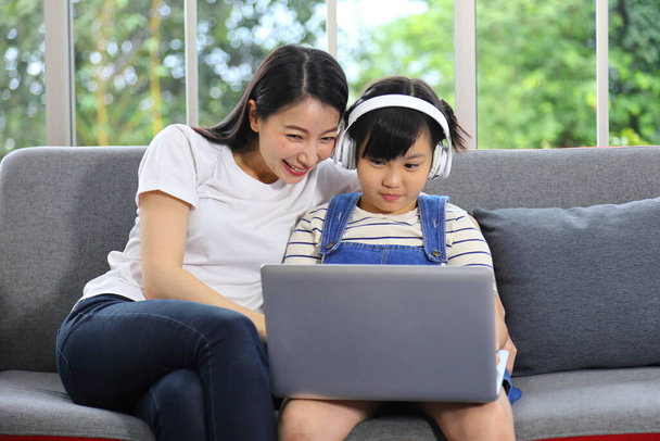 Mère asiatique enseignant à sa fille à apprendre de la classe en ligne en utilisant un ordinateur portable pour l'enseignement à domicile et le concept d'éducation - Photo, image