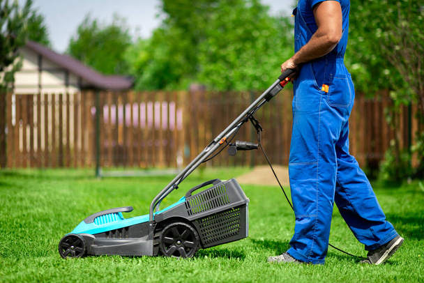 Çim biçme. Yeşil bir bahçede çim biçen bir işçi. Elektrikli çim biçme makinesi olan bir adam çimleri biçiyor. Bahçıvan bahçeyi buduyor. - Fotoğraf, Görsel