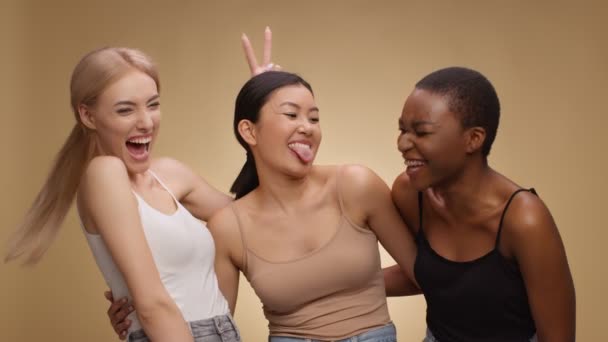 Drie gelukkige multi-etnische vrienden samen lachen, grimmig en steken tongen, beige achtergrond, slow motion - Video