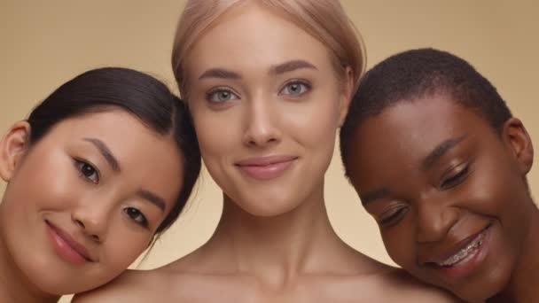 Variedad de belleza. Primer plano retrato de asiático, caucásico y africano americano damas abrazando y sonriendo a la cámara - Imágenes, Vídeo
