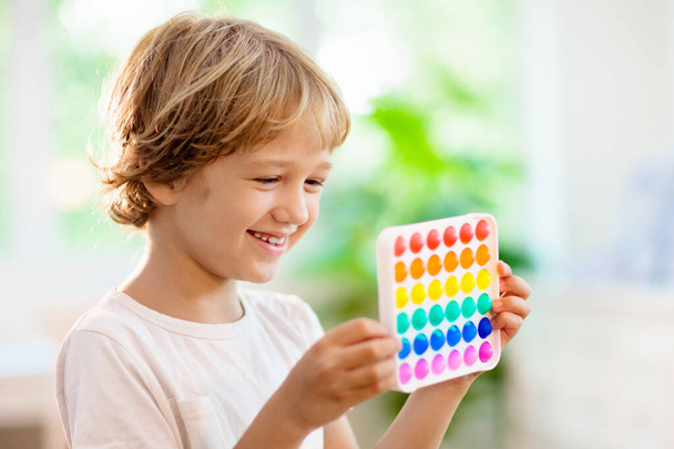 A gyerekek az érzékszervi játékkal játszanak. Stressz és szorongás csillapítás. Trendi szilícium fidgeting játék stresszes gyermekek és felnőttek. Puha, puha buborékos játékok. Gyerek játszik szivárvány színű pop-it. - Fotó, kép