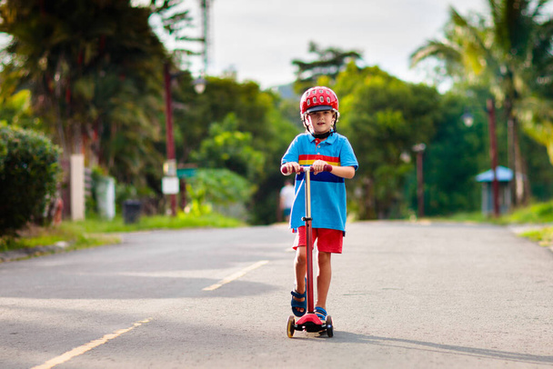 Little boy riding scooter. Kids ride kick board. Child playing on suburban street on sunny summer day. Safe helmet for children. Healthy outdoor activity. Cute kid on his way to school. - Photo, Image