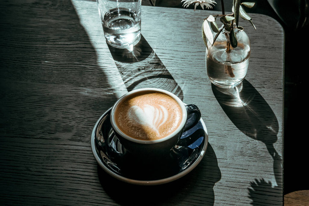 Café Cappuccino em mesa de madeira preta no café. Luzes e sombras, conceito de fotografia de bebidas alimentares. Lindo, calmo, saboroso, com mau humor atmosférico. Fechar, vista superior - Foto, Imagem
