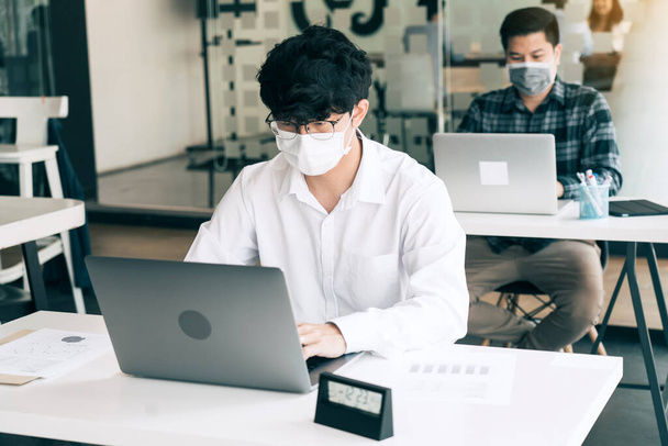 colega asiático trabalha enquanto vestindo uma máscara no escritório durante COVID-19. - Foto, Imagem