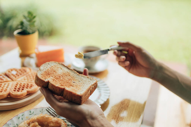Knife spreading butter on toast bread in hands in the morning breakfast. Coffee and dessert concept. - Foto, imagen