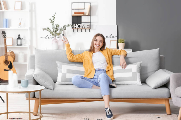 Beautiful young woman with air conditioner remote control in living room - Valokuva, kuva