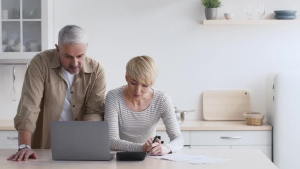 Mature Couple Calculating Expenses Taking Notes Planning Budget In Kitchen - Footage, Video